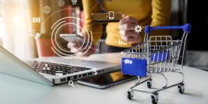 Personne sur un ordinateur et téléphone avec petit caddie sur le bureau